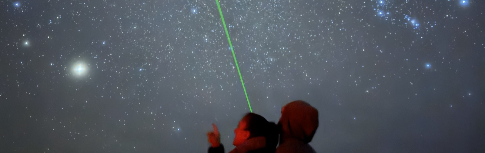 Tour guests beneath a dense starfield as a guide's green laser traces constellations overhead